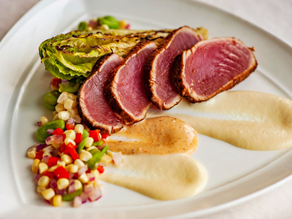 The image shows a plated dish featuring seared tuna slices with grilled greens, colorful diced vegetables, and two types of sauces arranged artfully.