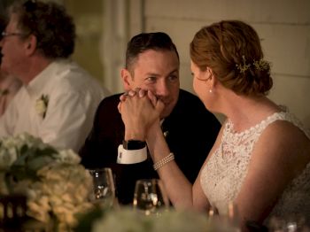 A couple in wedding attire holds hands and gazes at each other lovingly during a reception.