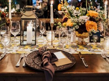 A beautifully set dining table with candles, flowers, wine glasses, and neatly arranged utensils, creating a warm and elegant ambiance.