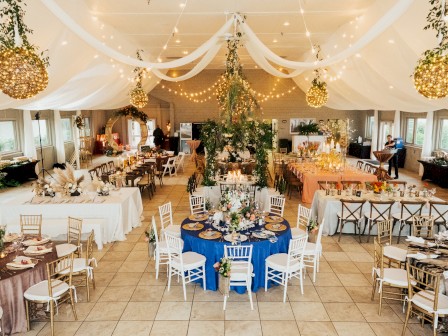 A decorated banquet hall with round and rectangular tables adorned with flowers and lights, and hanging greenery and lights from the ceiling.