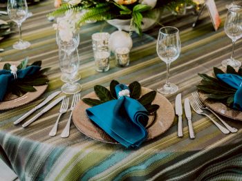 A beautifully set table with a striped tablecloth, blue napkins, wine glasses, cutlery, and floral centerpieces, ready for a formal meal.