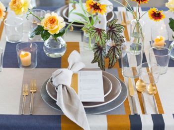 A beautifully set table with striped tablecloth, flowers in vases, candles, cutlery, plates with napkins, and glasses. A menu is placed on each plate.