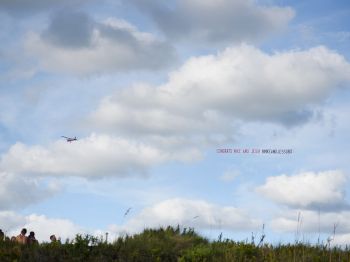 A small airplane flies in the sky with a banner reading 