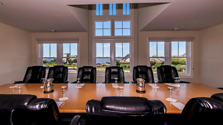 A conference room with a long table, leather chairs, notepads, pens, and drinks, with a scenic outdoor view through large windows at the end of the sentence.