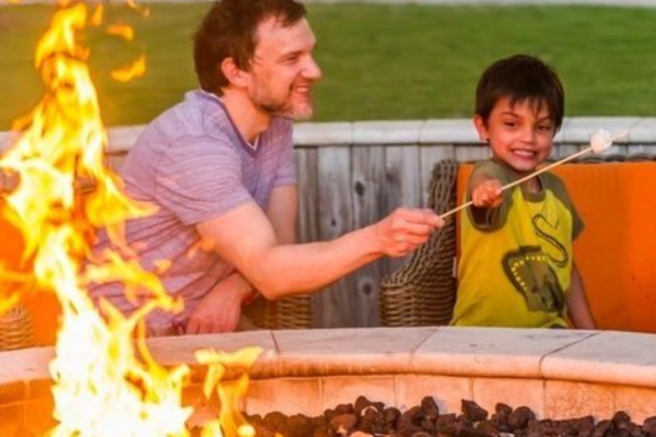 A man and a child are toasting marshmallows over an outdoor fire pit, smiling and enjoying the activity together.