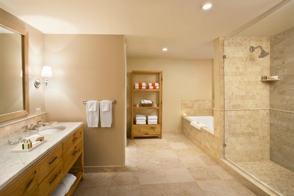 The image shows a bathroom with a double sink vanity, a glass-enclosed shower, a bathtub, and a shelf with towels and toiletries.