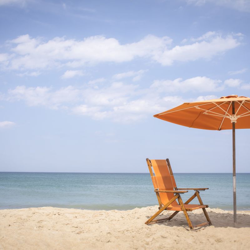 A beach scene with an orange chair and umbrella on the sand next to the tranquil sea under a partly cloudy sky.