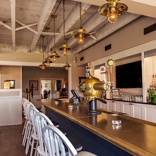 The image shows a cozy bar with a brass countertop, high chairs, liquor bottles, and warm lighting, creating an inviting atmosphere for patrons.