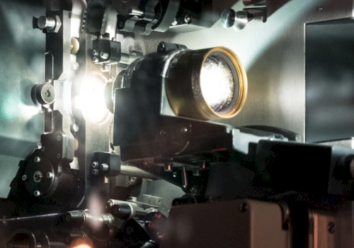 This image shows a close-up of a film projector's mechanism, with light passing through lens components, suggesting it's actively projecting.