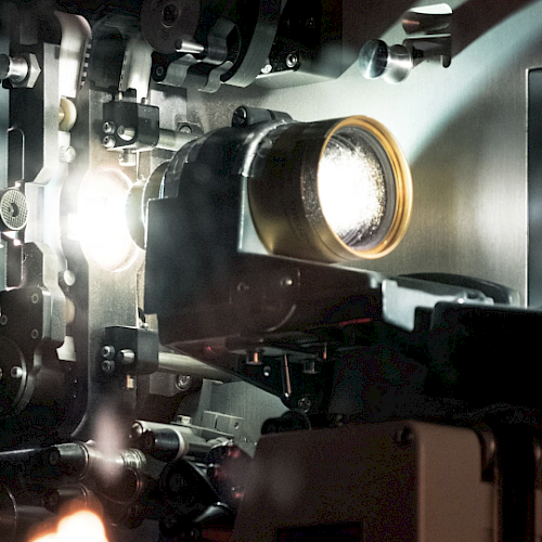 This image shows a close-up of a film projector's mechanism, with light passing through lens components, suggesting it's actively projecting.