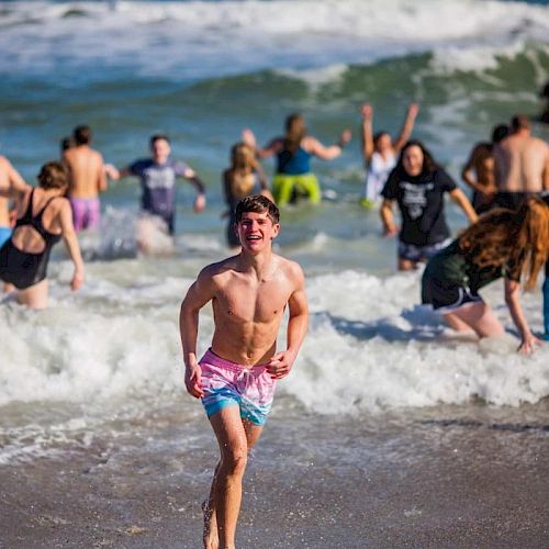 People enjoying a day at the beach, playing in the waves and sand, with a young man running towards the shore.