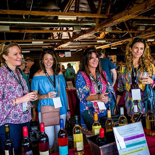 A group of women tasting and discussing wines at an indoor event with bottles displayed on a table.