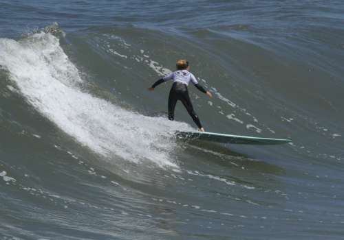 A person wearing a wetsuit is surfing on a wave, riding towards the left side of the image.