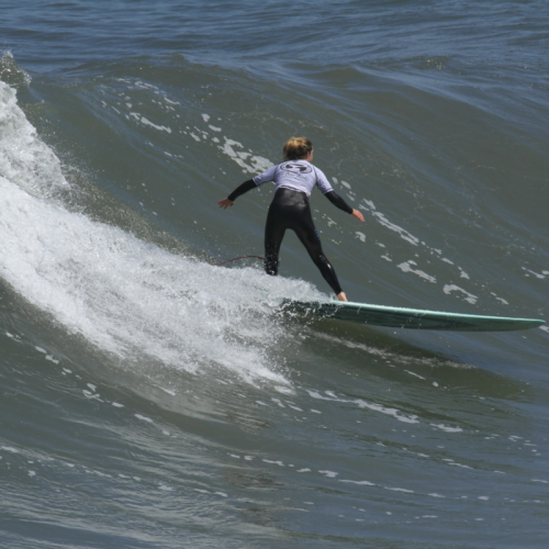 A person wearing a wetsuit is surfing on a wave, riding towards the left side of the image.