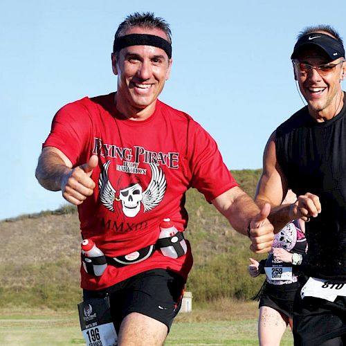 Two people are running enthusiastically outdoors. One wears a red shirt and the other in black. A monument is seen in the background.