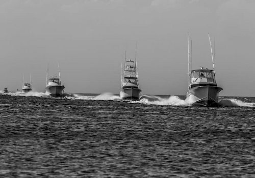 The image shows four motorboats speeding on the water in a single file line, creating waves behind them.