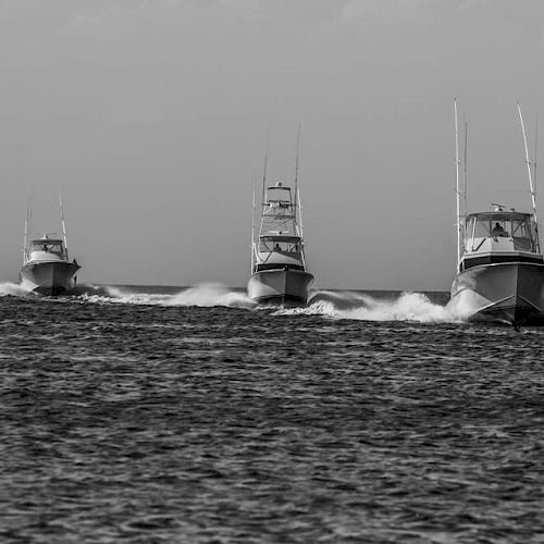 The image shows four motorboats speeding on the water in a single file line, creating waves behind them.