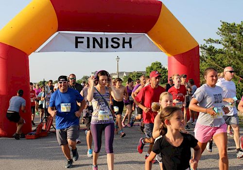 People are running and walking through a finish line of a race under a large inflatable arch marked 