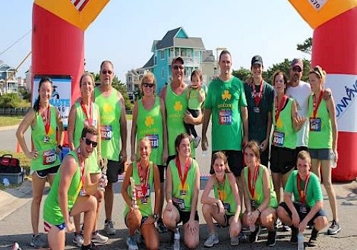 A group of people in matching green shirts and medals pose under an archway with flags, seemingly after completing a race.