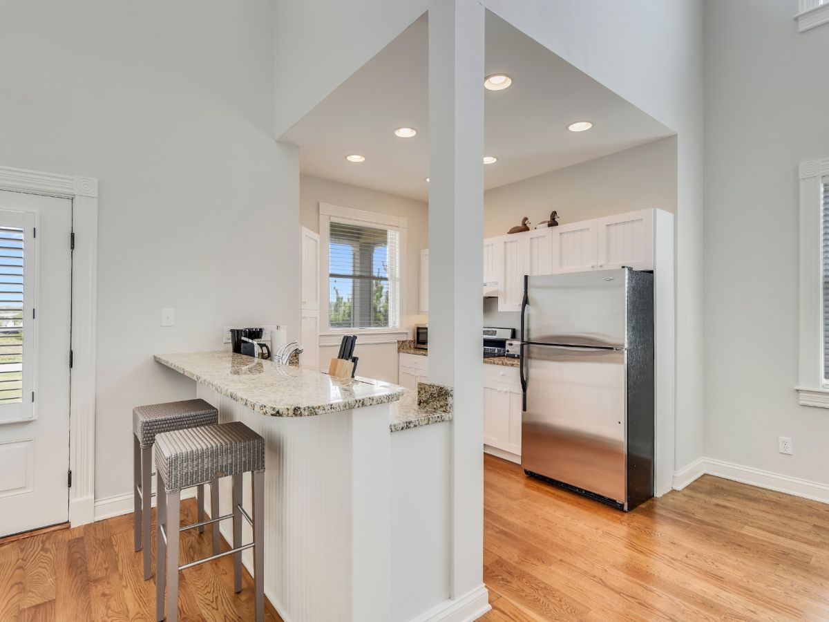 A modern kitchen with white cabinets, stainless steel appliances, and a breakfast bar with two stools, on a hardwood floor ending the sentence.