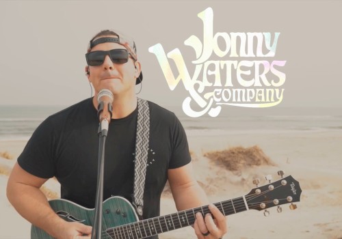 A man in sunglasses plays guitar and sings with a mic on a beach. The text overlay reads 
