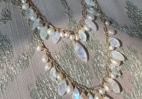A necklace with two layers features a mix of pearlescent and translucent gemstones on a light-colored fabric background.