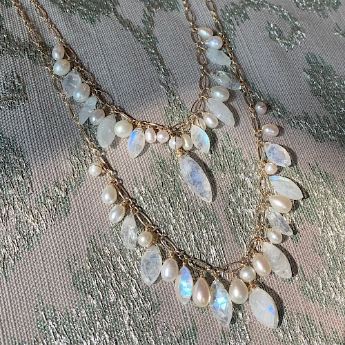 A necklace with two layers features a mix of pearlescent and translucent gemstones on a light-colored fabric background.