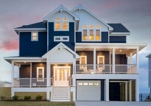 A three-story house with a white and dark blue exterior, large windows, multiple balconies, and a garage, set against a twilight sky.