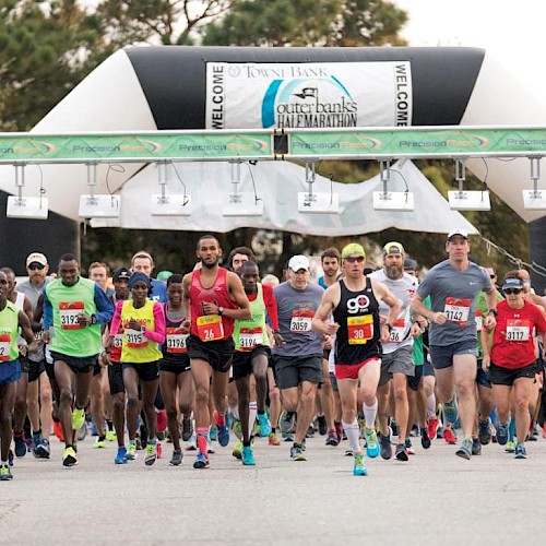 A group of runners starting a marathon, passing under an inflatable archway with 