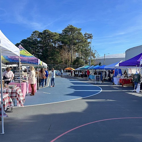 People are attending an outdoor market with various booths and tents under a clear blue sky.