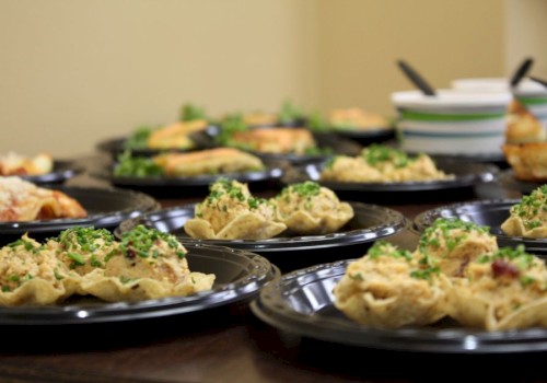 The image shows multiple black plates with a variety of food items, including stuffed pasta shells and salads, set on a table.