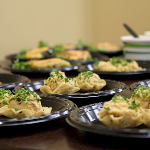 The image shows multiple black plates with a variety of food items, including stuffed pasta shells and salads, set on a table.