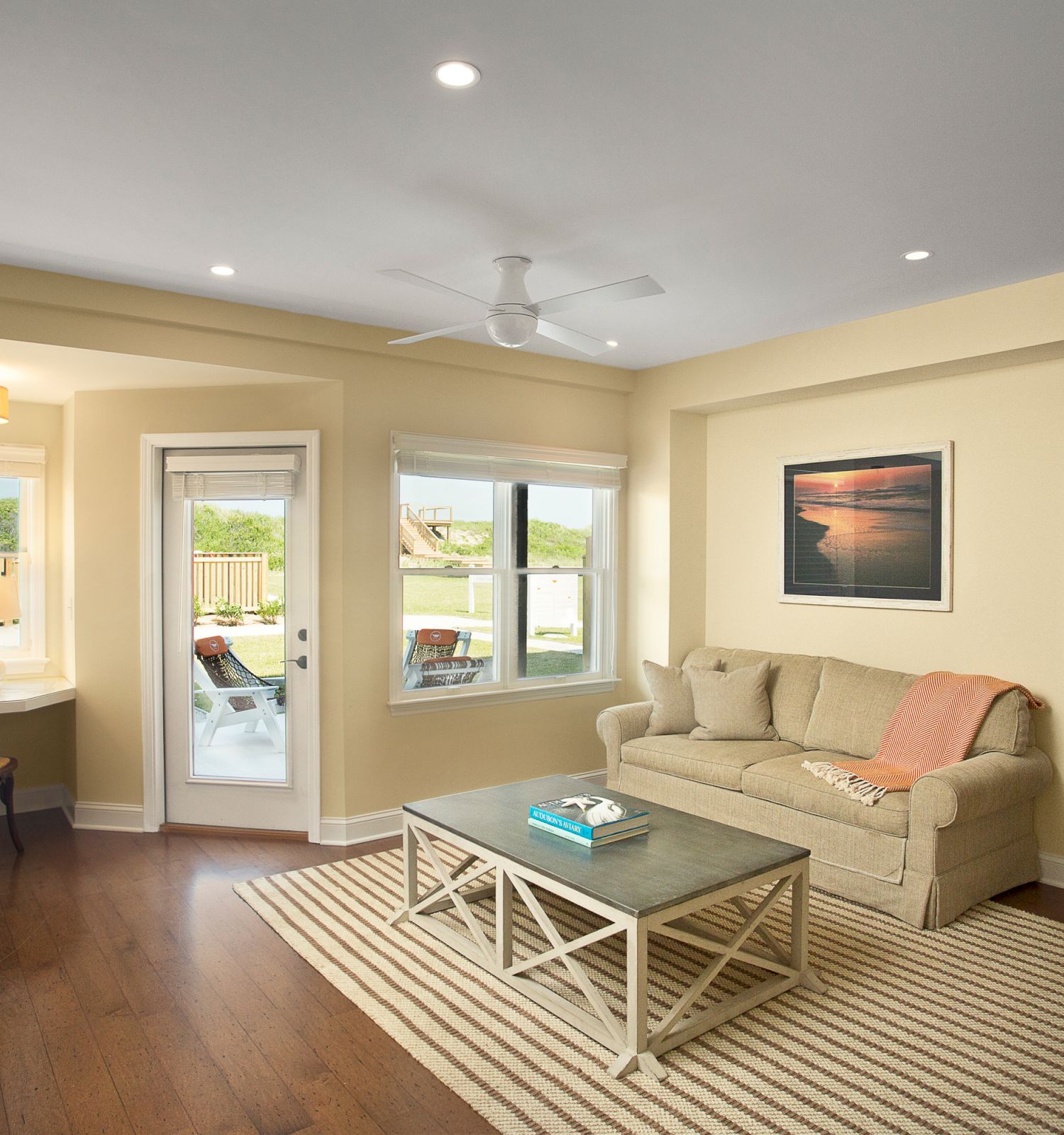 This image shows a cozy, modern living room with a sofa, coffee table, TV, and art. The space leads to a bedroom and a small study nook.