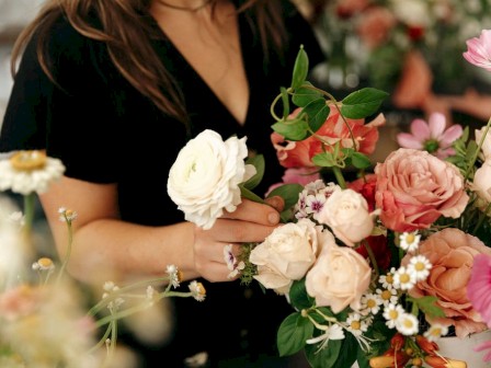 A person arranging a variety of colorful flowers, including roses and daisies, creating a floral display.