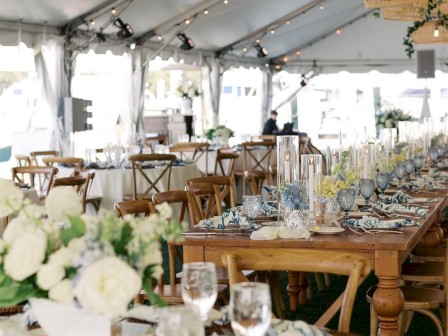 A beautifully decorated event tent with elegant tables set for dining, featuring floral centerpieces and hanging lights.