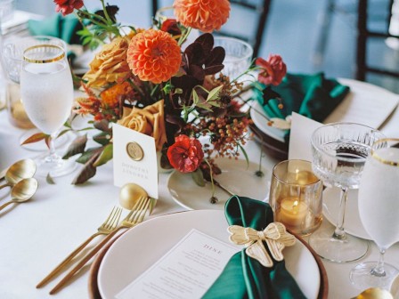 A beautifully set table with a floral centerpiece, green napkins, gold utensils, menus, and glasses.