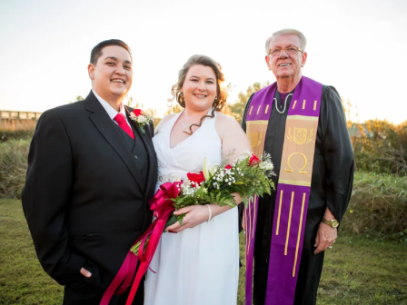 A wedding ceremony with a couple and a priest standing outdoors, with the couple holding a bouquet of flowers.